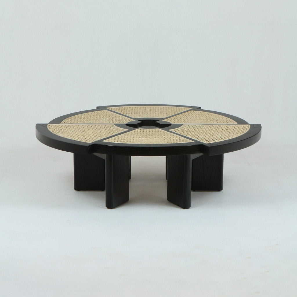 Low round coffee table with natural woven cane panels arranged in radial segments set into a dark-stained oak frame, featuring a central circular opening and short chunky black wood legs.