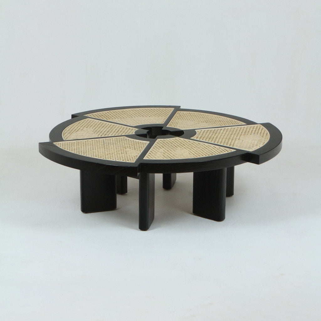 Low round modern coffee table with a black stained solid-wood frame and six natural cane-woven wedge panels in the tabletop, featuring a central circular cutout and short rectangular slab legs.