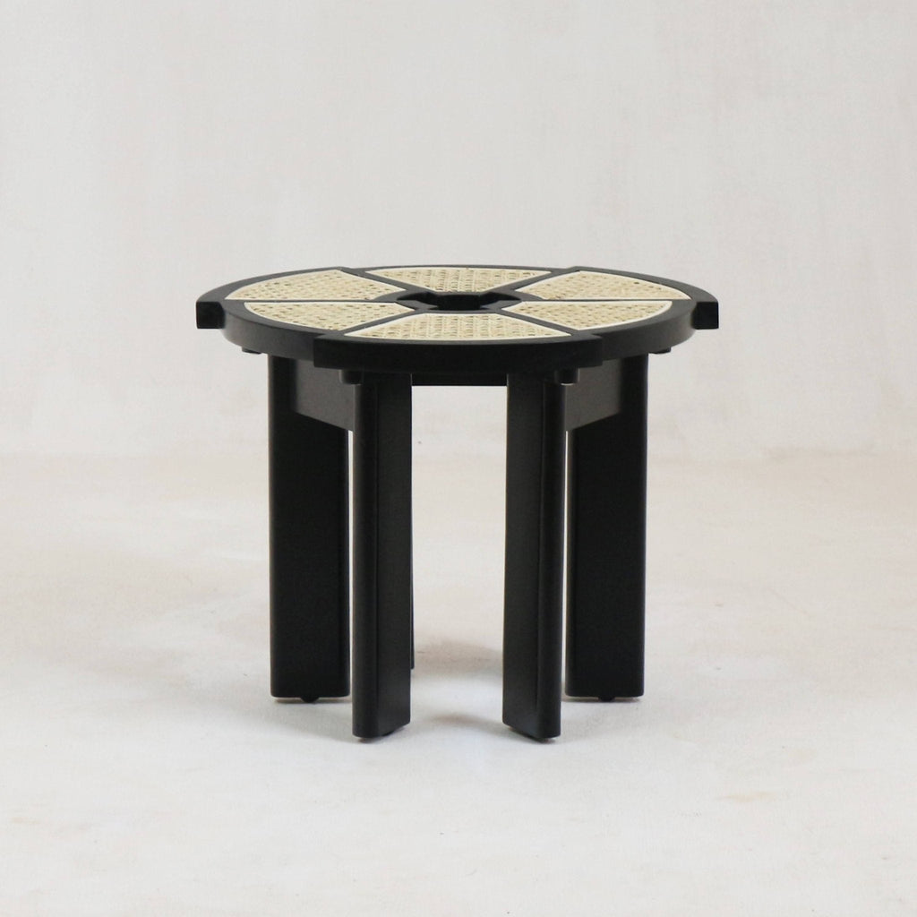 Round modern side table with glossy black solid-wood frame and natural cane-woven segmented top, supported by clustered vertical black wood legs.