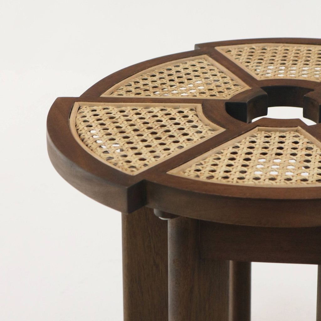 Close-up of a round modern side table top in medium brown teak with natural cane inlay set into a segmented solid wood frame, showing the central cutout and cylindrical legs.