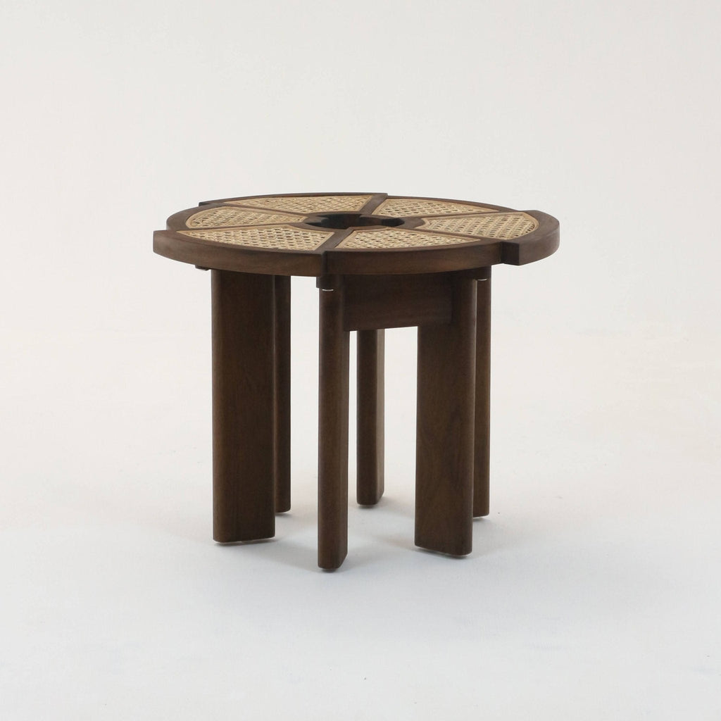 Round teak side table with medium-brown solid wood frame, four radial woven cane panels and a central circular cutout, supported by grouped rounded legs for a modern mid-century look.