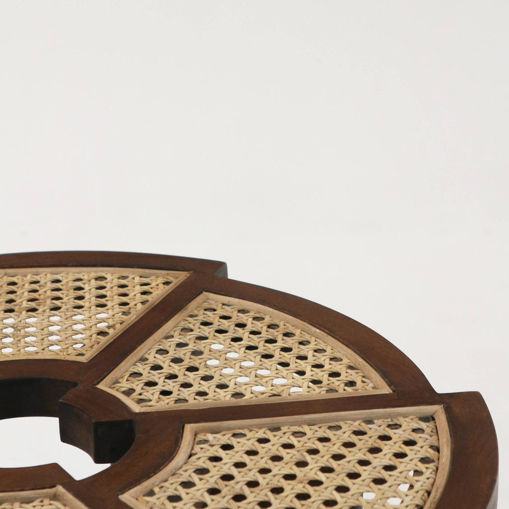 Close-up of a medium-brown teak side table top featuring natural rattan cane-woven panels set into a segmented wooden frame with a central circular cutout, highlighting the woven texture and warm wood grain.