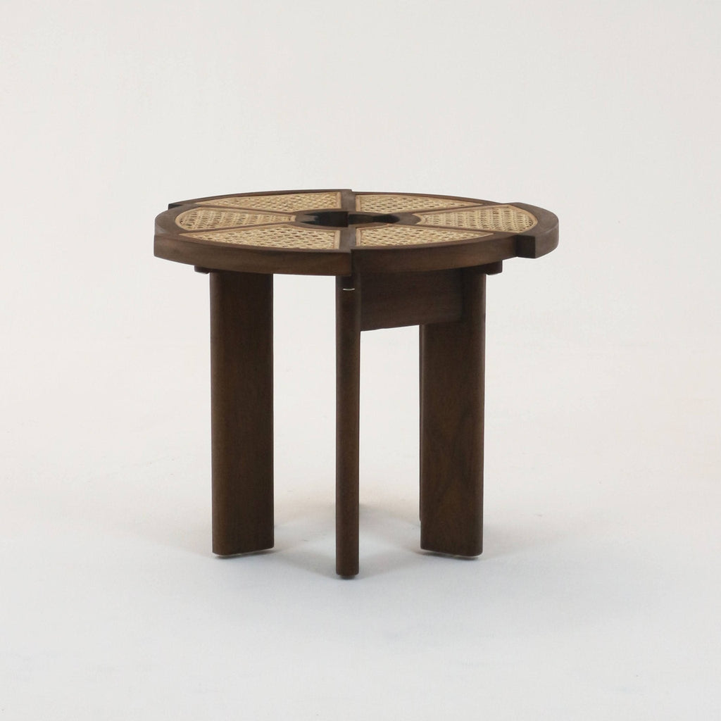 Medium brown teak side table with a round top featuring woven rattan cane in four pie-shaped panels and three solid wooden legs, photographed on a white studio background.