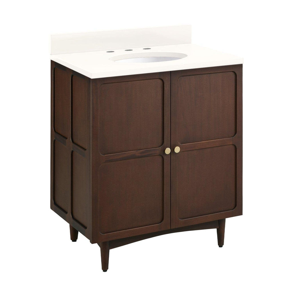Freestanding coastal-style single-sink bathroom vanity in dark solid wood with a white stone countertop and backsplash, oval sink cutout, two recessed-panel doors, small round brass knobs and tapered legs.