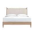 Front view of a mid-century modern teak platform bed with a cream woven rattan headboard, low teak frame and crisp white bedding.