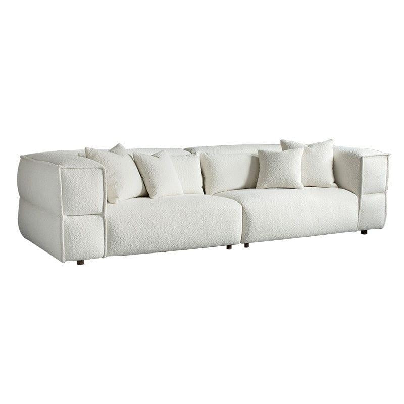 Low-profile white boucle sectional sofa with deep cushioned seats, rounded block arms, four matching throw pillows and short dark wooden legs on a white background.