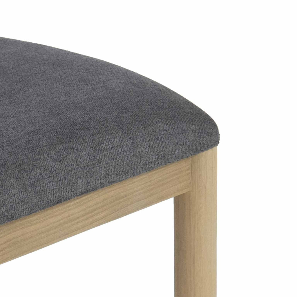 Close-up of a gray boucle upholstered seat cushion on a natural oak stool frame and rounded leg, highlighting the fabric texture and light wood grain.