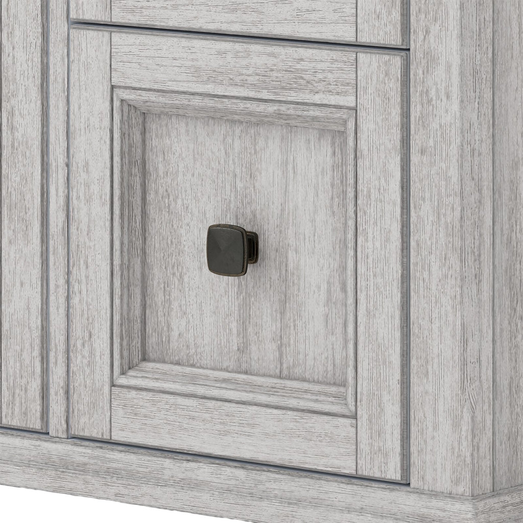 Close-up of a whitewashed solid wood bathroom vanity door with recessed paneling and a small square dark metal knob.