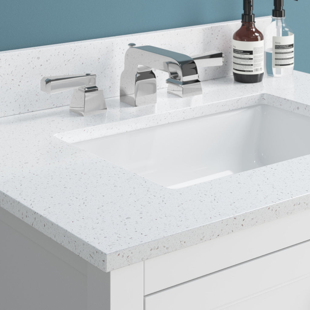 Close-up of a stone-colored speckled quartz vanity top with a white ceramic undermount rectangular sink, polished chrome widespread faucet and lever handles, two soap dispensers, and a modern white solid wood vanity against a blue wall.