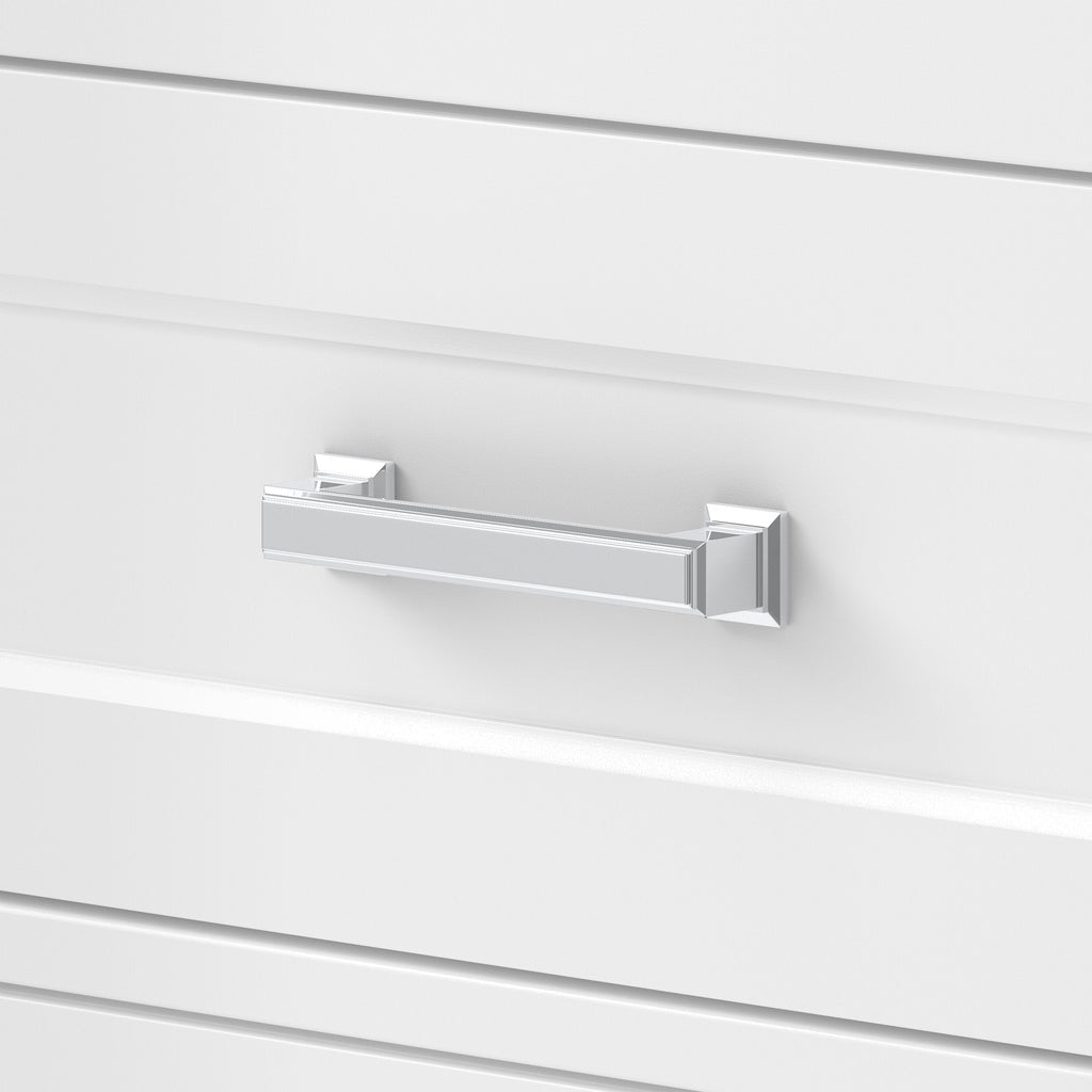 Close-up of a chrome rectangular bar drawer pull mounted on a white painted vanity drawer front with recessed panel detailing, shown on a modern solid wood single-sink vanity.