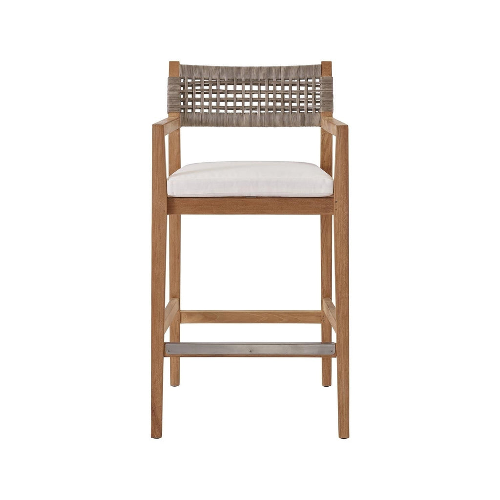 Coastal teak outdoor bar stool with a natural teak solid-wood frame, neutral woven rope back, white fabric upholstered seat cushion, armrests and a metal-reinforced footrest.