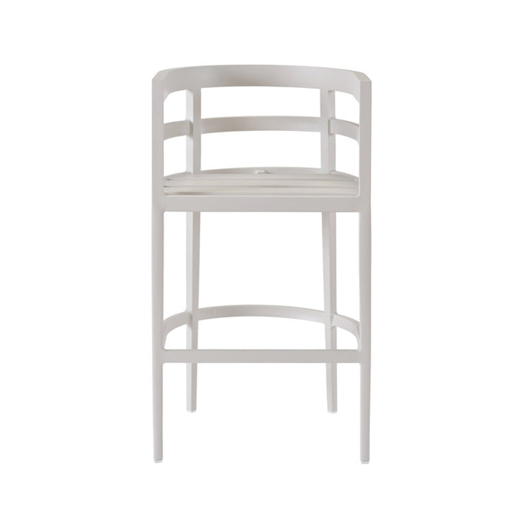 Front view of a coastal-style teak outdoor bar stool in a pale natural finish, with a slatted seat and thin upholstered cushion, curved slatted back with integrated armrests, slim tapered legs and a curved footrest.