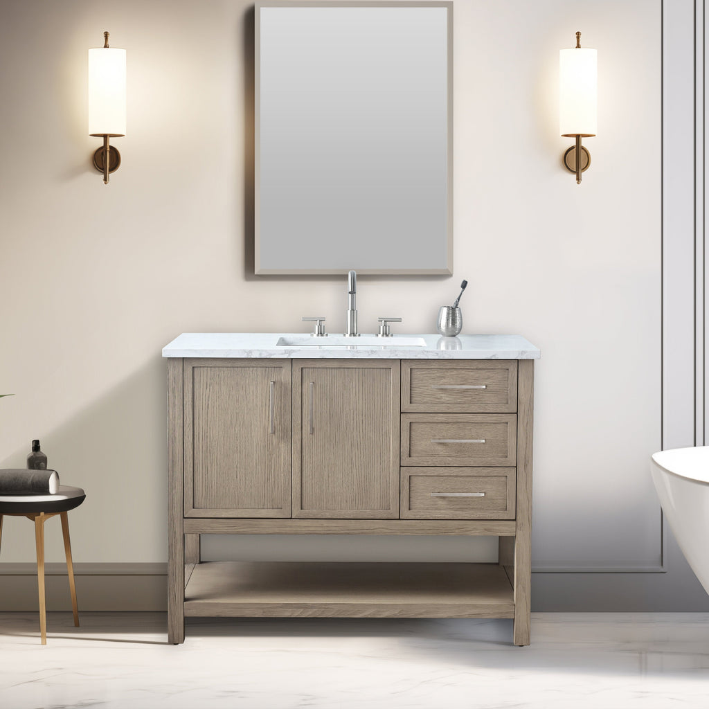 Modern 42-inch single-sink solid wood bathroom vanity in stone finish with marble top, undermount ceramic sink, chrome faucet, three right-side drawers, two cabinet doors, open lower shelf, and brass wall sconces beside a mirror.