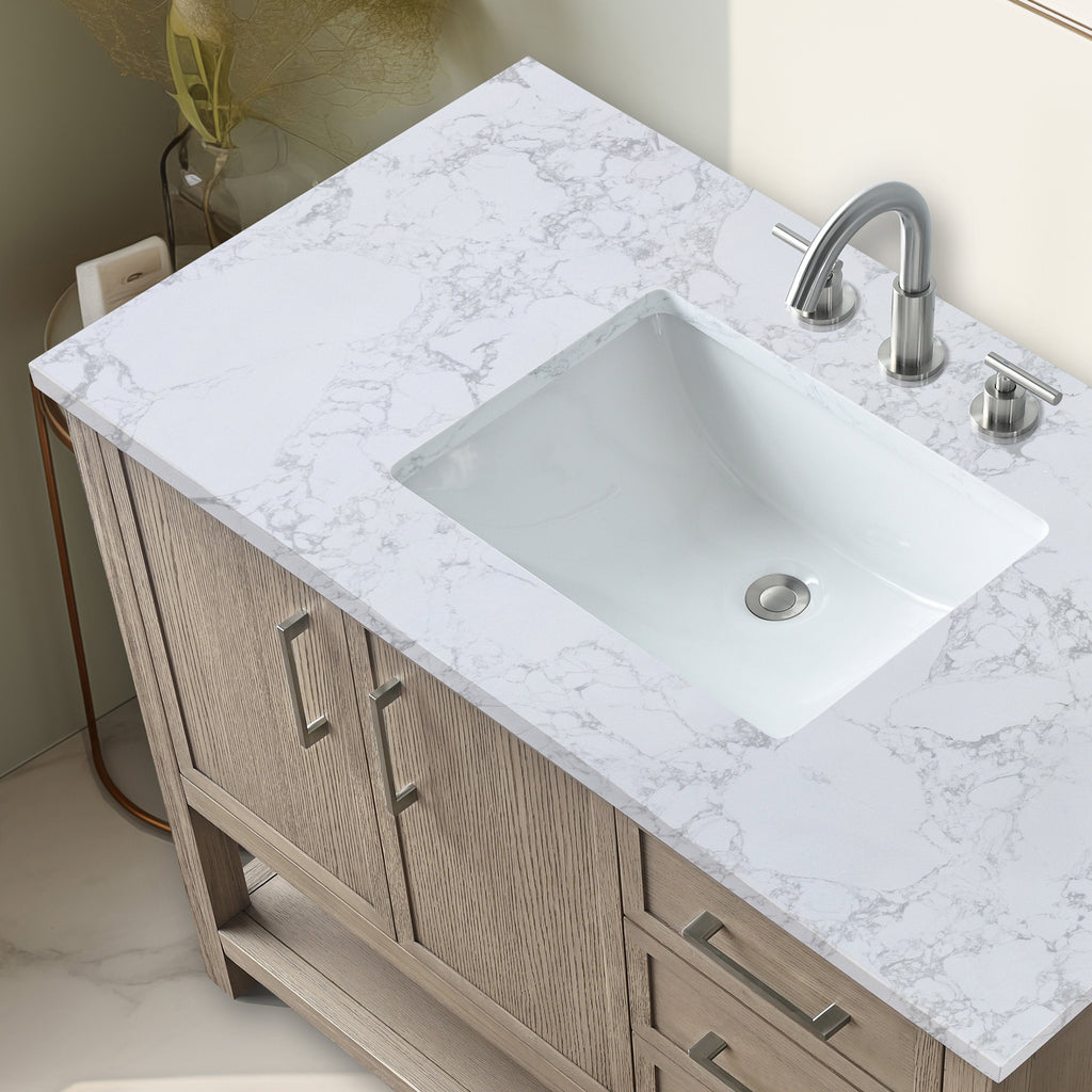 Top-down view of a modern single-sink bathroom vanity featuring a white marble-patterned stone top, rectangular undermount ceramic sink, brushed nickel faucet, and light oak solid wood cabinet with metal pulls.