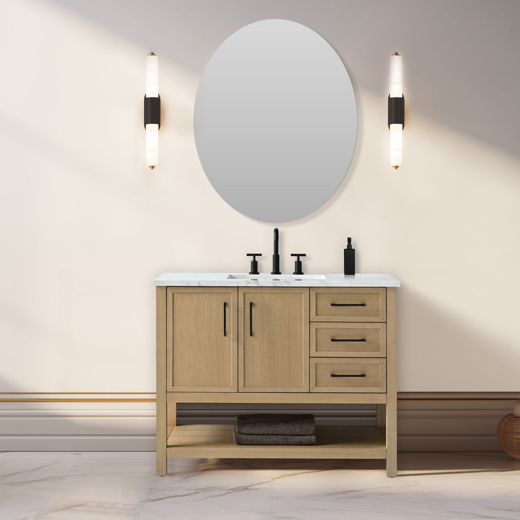 Freestanding 42-inch solid wood bathroom vanity with marble top, undermount ceramic sink, matte black faucet and hardware, two cabinet doors and three right-side drawers, open lower shelf with folded towels, round mirror and twin sconces.