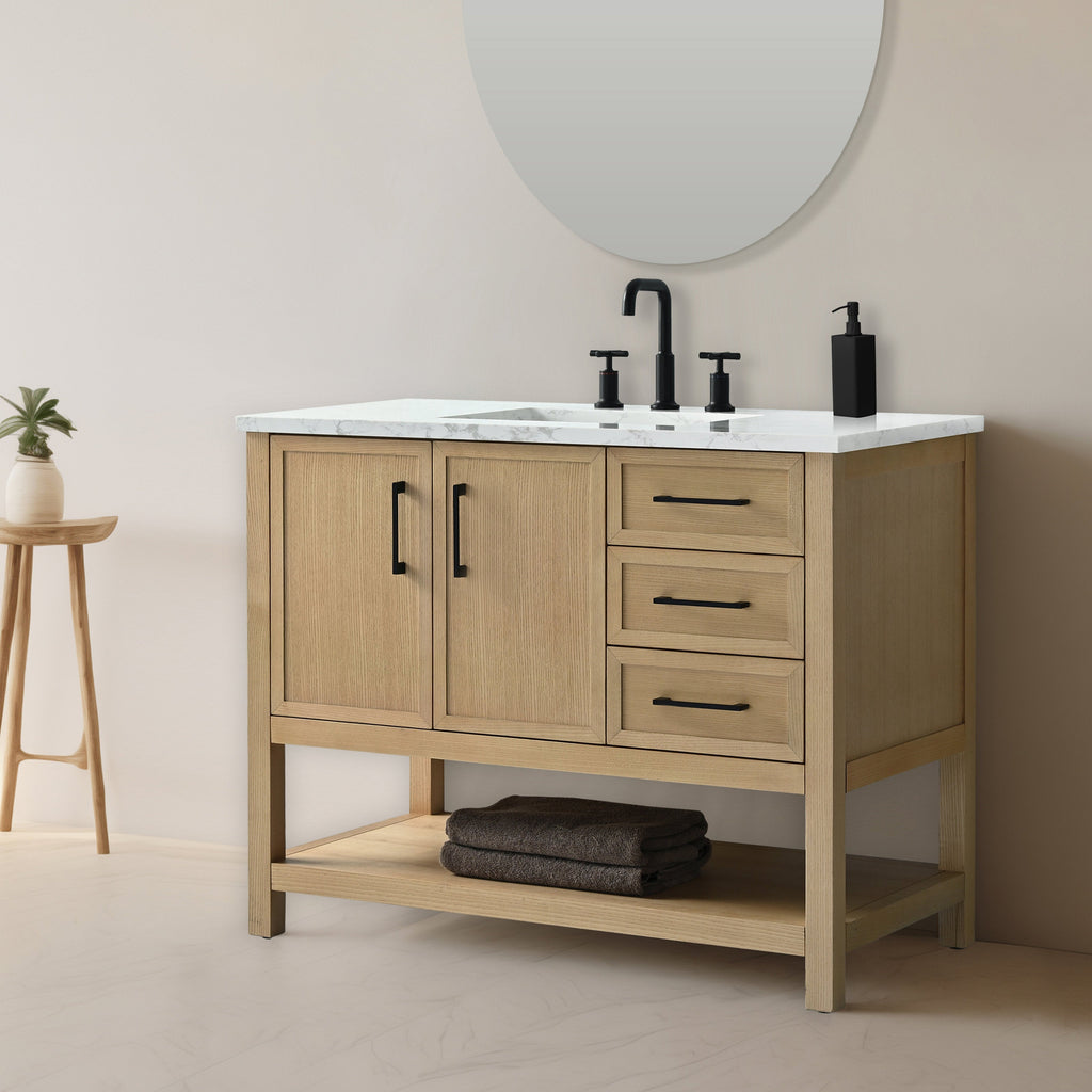 Modern 42-inch solid wood bathroom vanity with white stone marble top, matte black faucet and hardware, two-door cabinet, three drawers and an open lower shelf with folded towels, shown with round mirror and small plant.