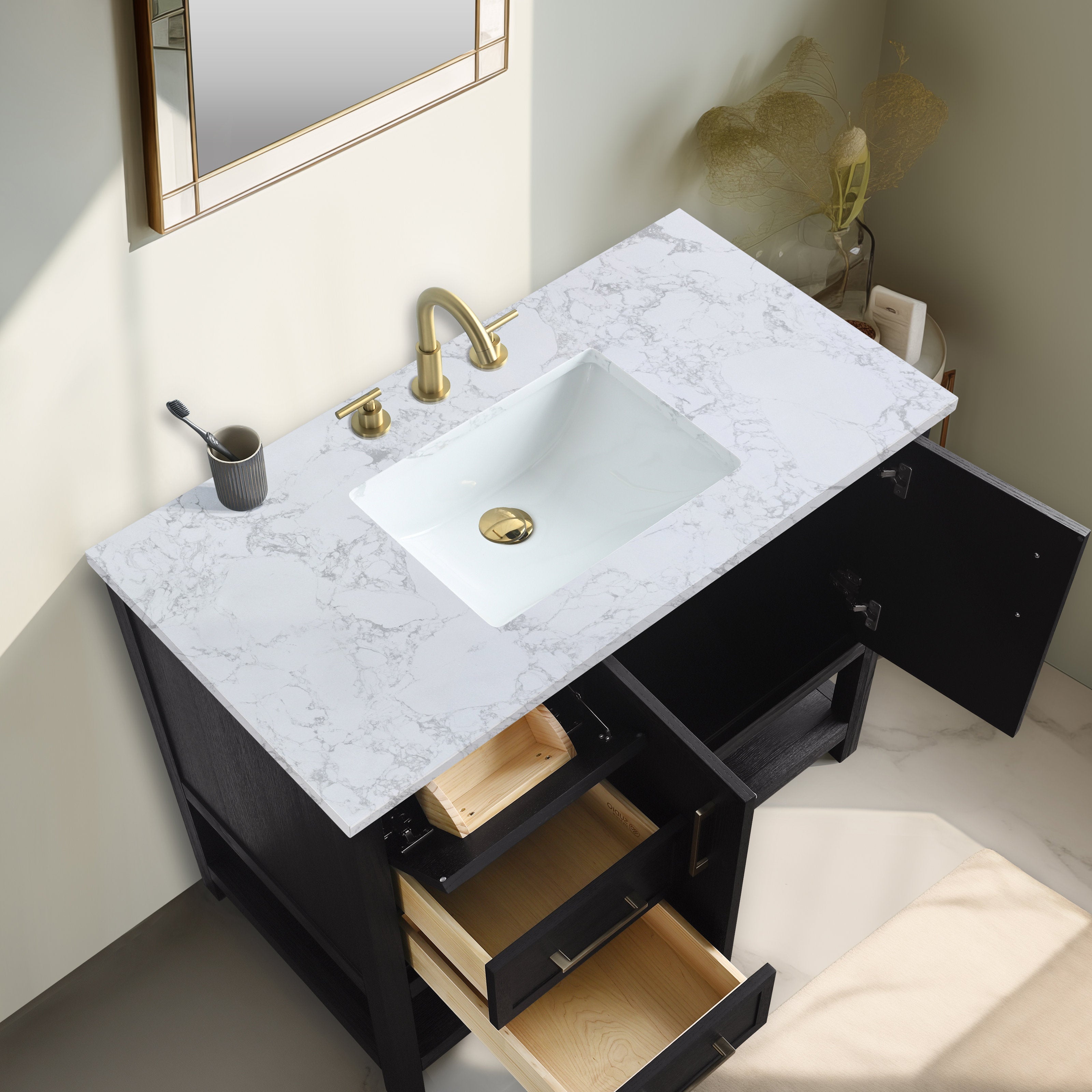Top-down view of a modern black solid-wood bathroom vanity with a white rectangular ceramic sink set into a stone marble-pattern countertop, brass faucet and drain, open drawers showing light wood interiors and an open cabinet door.