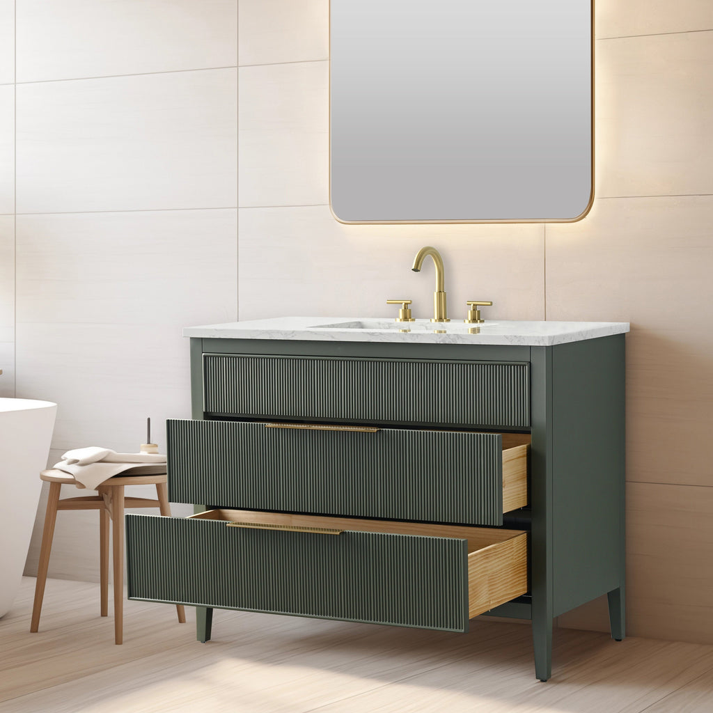 Modern single-sink bathroom vanity in stone-colored solid wood with fluted drawer fronts, white stone countertop and brass faucet; two drawers open to reveal natural wood interiors beneath a backlit mirror.