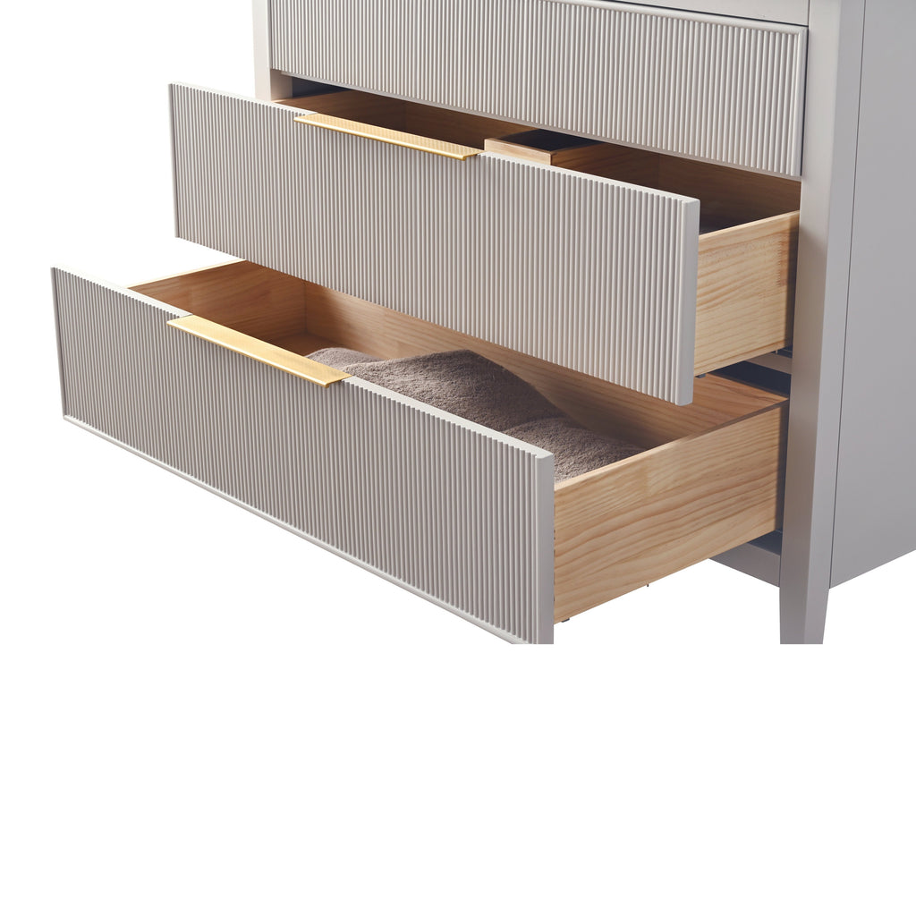 Close-up of a modern stone-colored bathroom vanity showing two open ribbed drawer fronts with solid wood interiors and gold-tone pulls; the lower drawer holds a folded taupe towel.