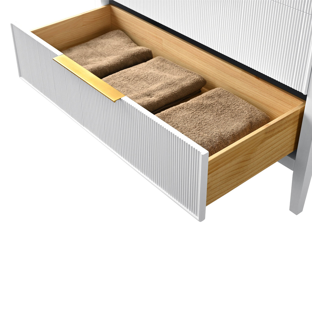 Open vanity drawer with a white fluted front and brass-tone handle revealing a natural solid wood interior holding three folded brown towels, detail of a modern single-sink bathroom vanity.