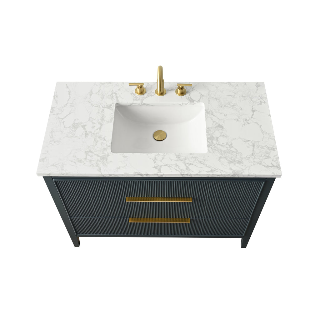 Modern single-sink bathroom vanity with white stone-pattern countertop, integrated rectangular white ceramic sink, brushed gold faucet and drain, and long gold drawer pulls on a dark fluted wood front.