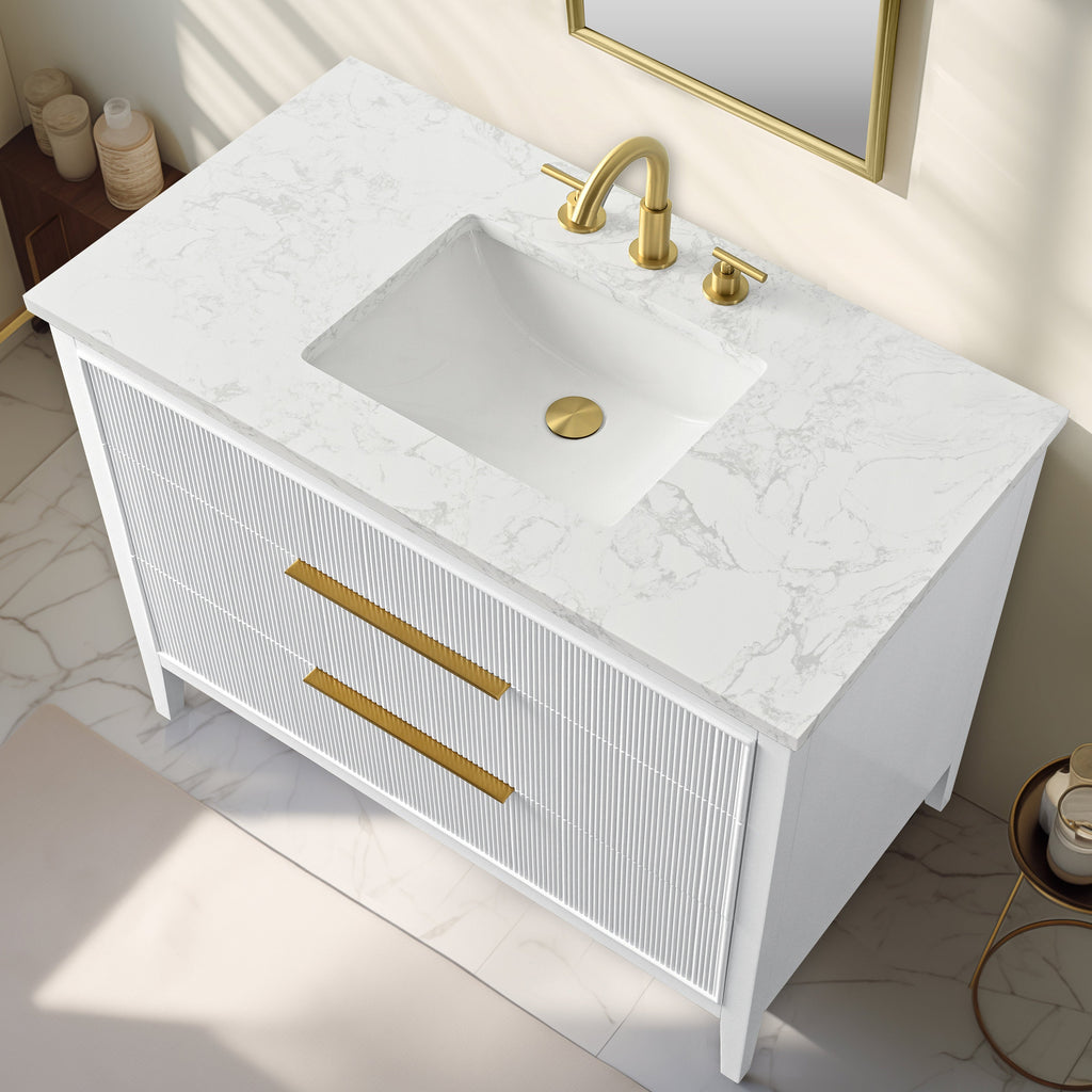 Top-down view of a modern white solid-wood bathroom vanity with a stone-look marble top, rectangular undermount ceramic sink, and brushed gold faucet and matching gold drawer pulls on fluted drawer fronts.