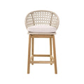 Front-facing armless outdoor bar stool with a natural teak wood frame, woven rope backrest and a light neutral fabric seat cushion, shown against a white background.