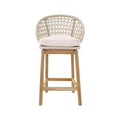 Front-facing armless outdoor bar stool with a natural teak wood frame, woven rope backrest and a light neutral fabric seat cushion, shown against a white background.