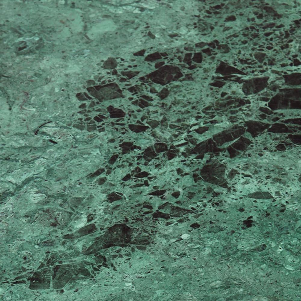 Close-up of a green marble tabletop with deep black veining and scattered stone fragments on a polished surface, highlighting the modern coffee table's natural stone texture.