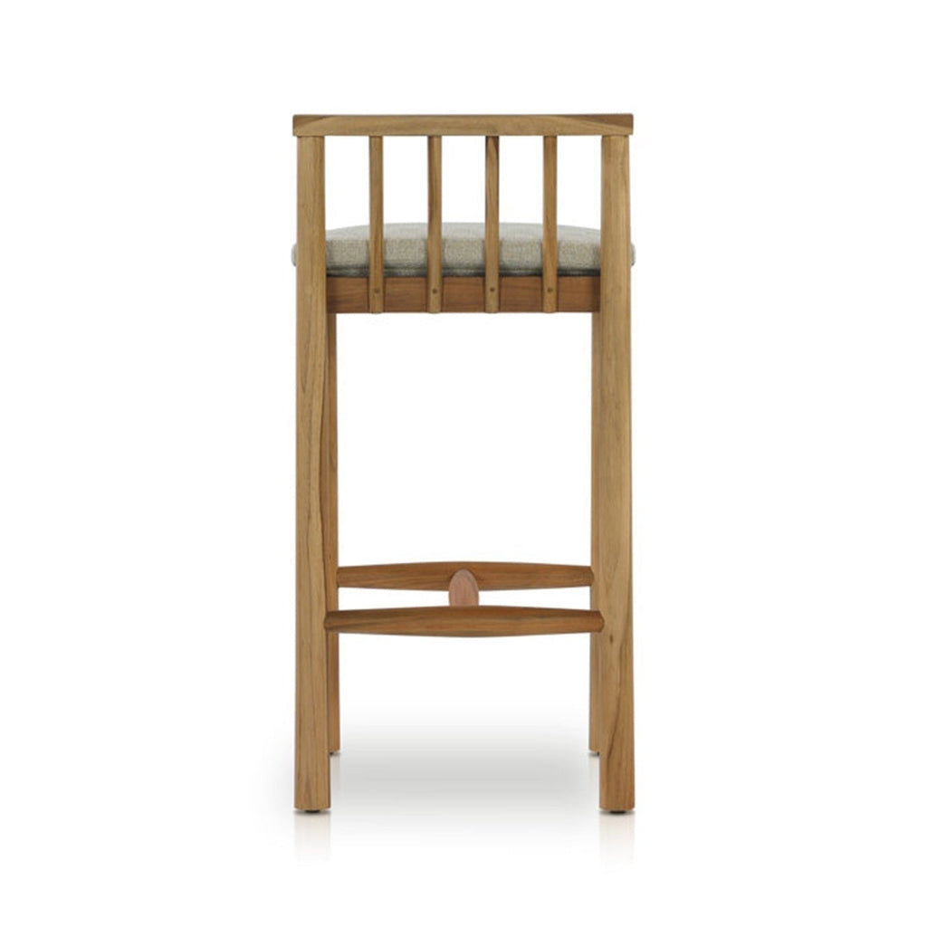 Rear view of an armless outdoor bar stool in natural teak with a light-gray upholstered seat, vertical slatted back and curved teak footrest in a coastal contemporary style.