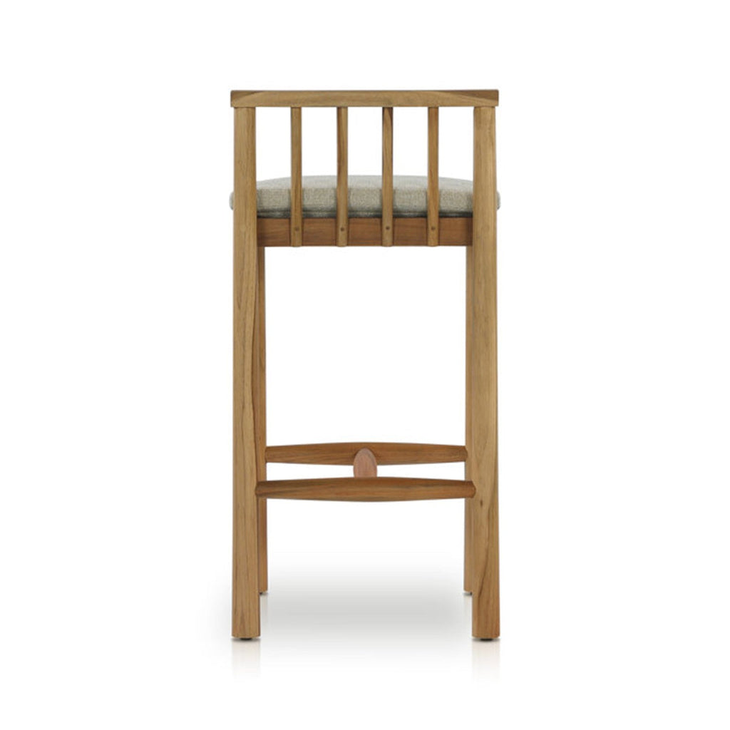 Rear view of an armless outdoor bar stool in natural teak with a light-gray upholstered seat, vertical slatted back and curved teak footrest in a coastal contemporary style.