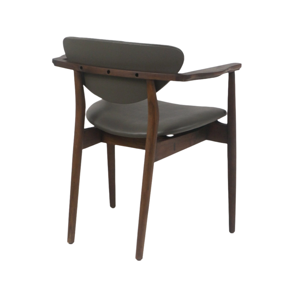 Rear three-quarter view of a mid-century modern dining chair with a teak wood frame, tapered legs and curved armrests, upholstered in dark gray leather on the seat and back.