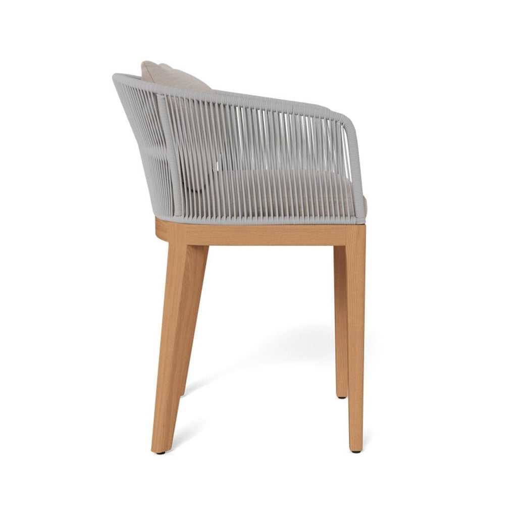 Side view of a coastal-style outdoor bar stool with a teak wood frame, light gray rope-wrapped back and arms, and beige upholstered fabric seat and back cushions.