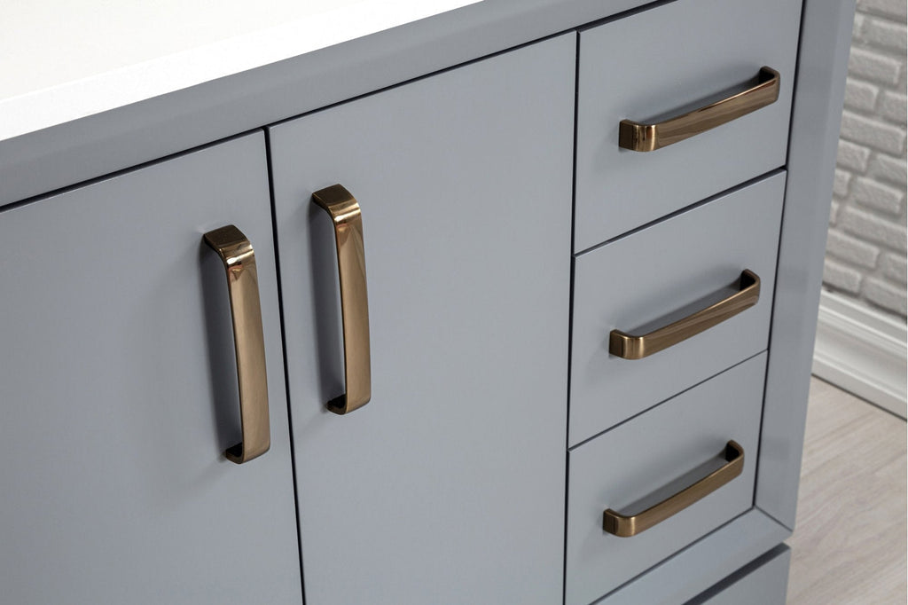 Close-up of a modern stone-colored solid wood bathroom vanity showing matte gray-blue cabinet doors and stacked drawers with brushed brass handles and a white stone countertop edge.