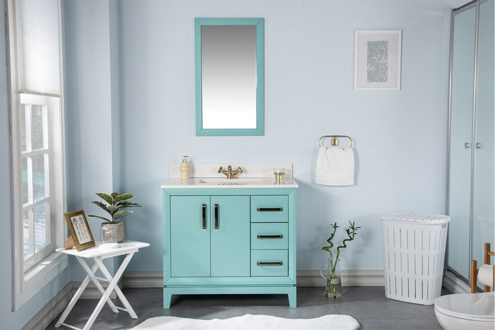 Turquoise single-sink solid wood vanity with a white stone countertop, brass faucet and hardware, matching turquoise framed mirror above, three drawers, towel ring and laundry basket in a modern bathroom setting.