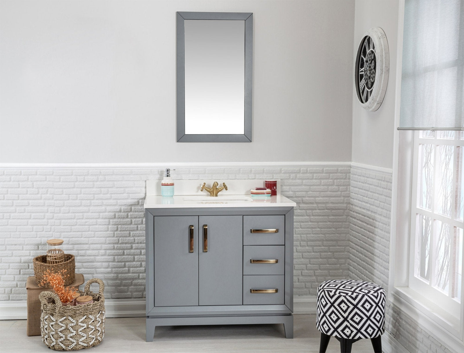 Modern gray solid-wood single-sink vanity with a white stone top, gold-tone faucet and hardware, three drawers and double doors, shown with a mirror above, woven baskets and a patterned stool in a bright bathroom.