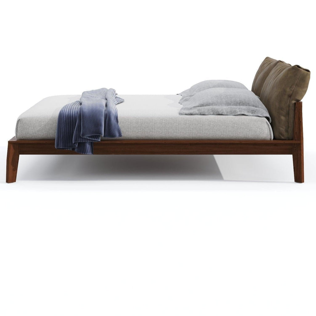 Side view of a mid-century modern teak king-size platform bed with a solid wood low-profile frame, light gray bedding, blue ribbed throw draped on the mattress, and an olive-brown cushioned headboard.