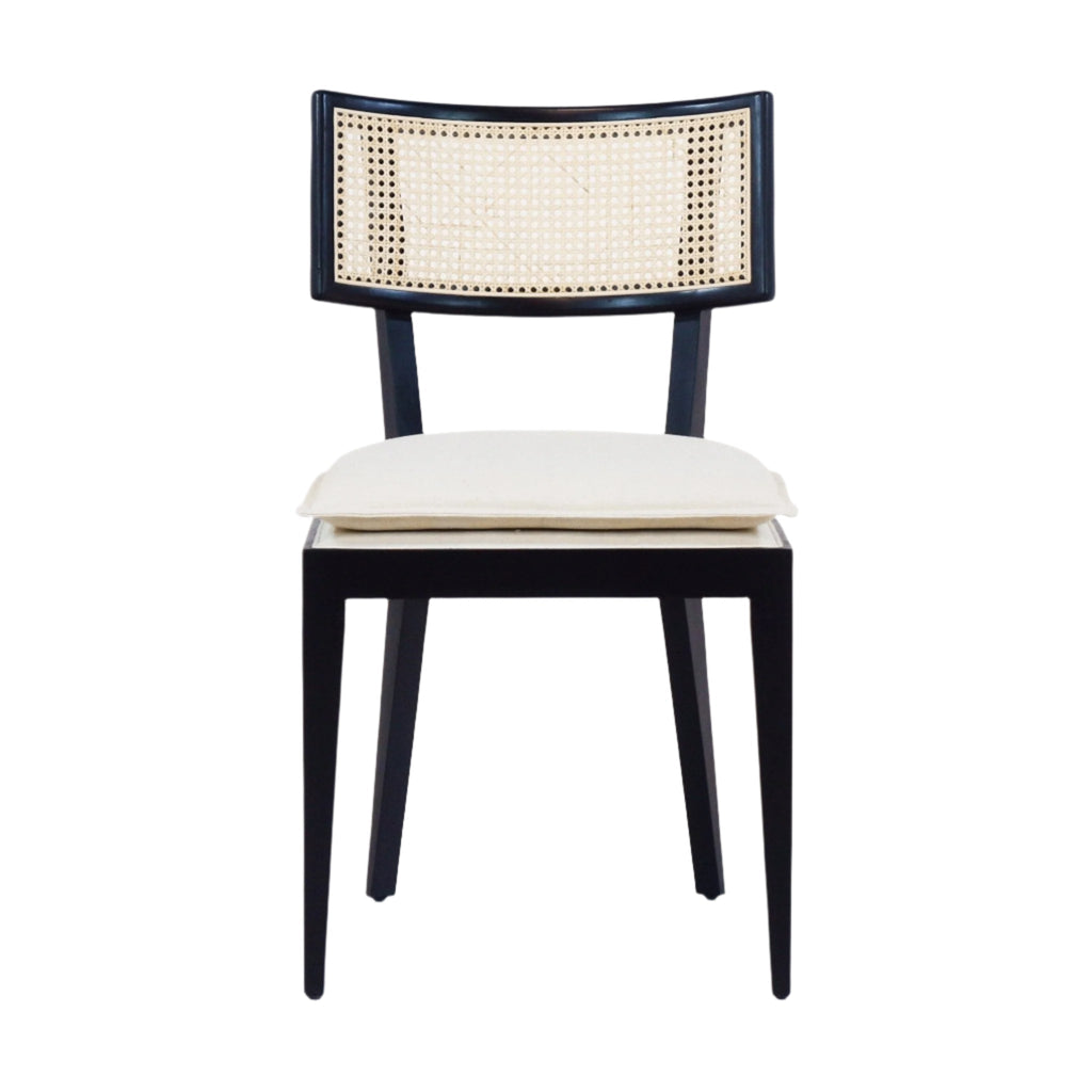 Front view of an armless black solid wood dining chair with a natural rattan cane backrest and a cream upholstered seat cushion, mid-century boho style, on a white background.