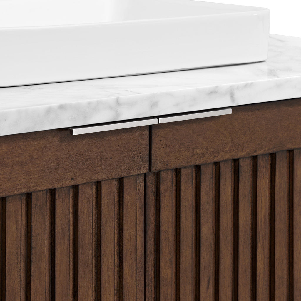 Close-up of a white ceramic vessel sink on a stone Calacatta marble top above a fluted natural wood vanity with vertical slats and slim brushed metal handles in a modern contemporary style.