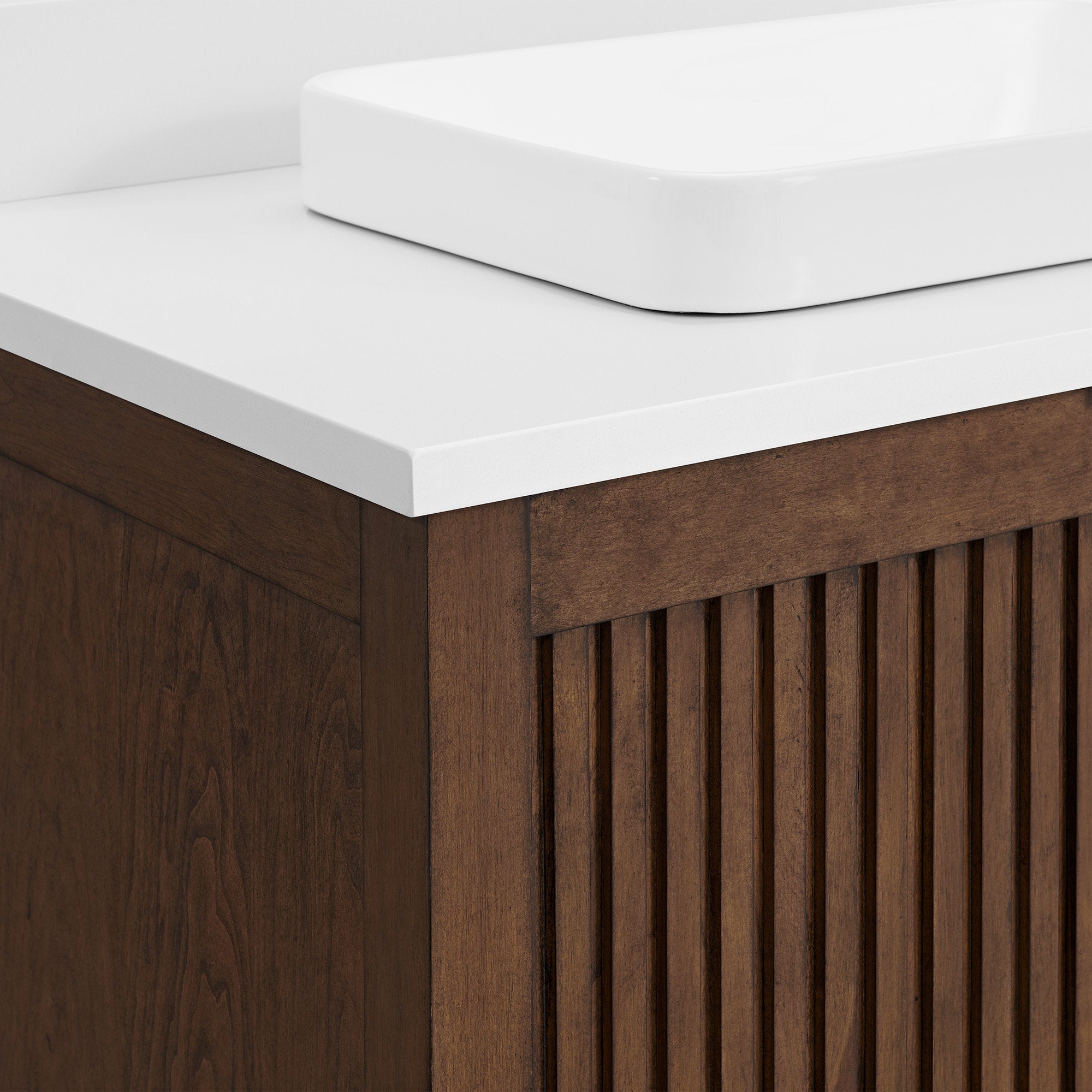 Close-up of a modern fluted solid wood bathroom vanity corner showing a warm brown wooden cabinet with vertical slatted front, a white stone countertop and a rectangular white ceramic vessel sink.