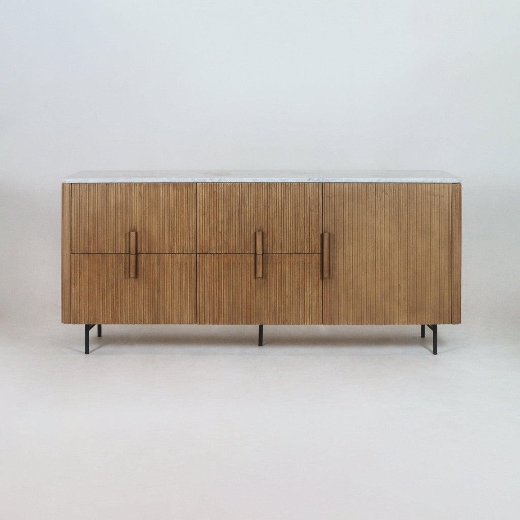 Long teak sideboard with vertical fluted front panels, a white marble top and slim black metal legs, photographed against a neutral studio background.