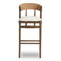 Front view of a natural wood counter stool with a woven rope C-shaped backrest and an off-white cushioned fabric seat tied to a slim rustic farmhouse-style frame.