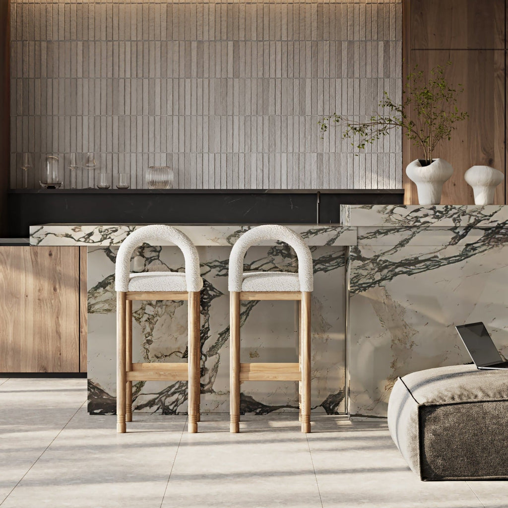 Two beige boucle bar stools with arched backs and natural oak legs sit at a veined marble kitchen island in a contemporary neutral kitchen.