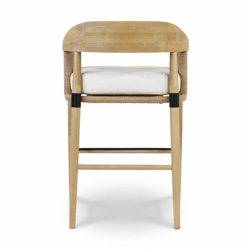 Rear view of a natural teak-framed bar stool with woven rope back, white fabric seat cushion, tapered natural wood legs, and black metal footrest and leg collars.