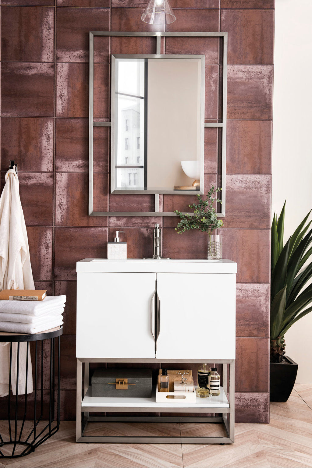 Contemporary white 31.5-inch single-sink solid wood bathroom vanity with stone countertop and integrated ceramic basin, stainless-steel legs and handles, rectangular framed mirror against textured brown tile wall with plant and towels.