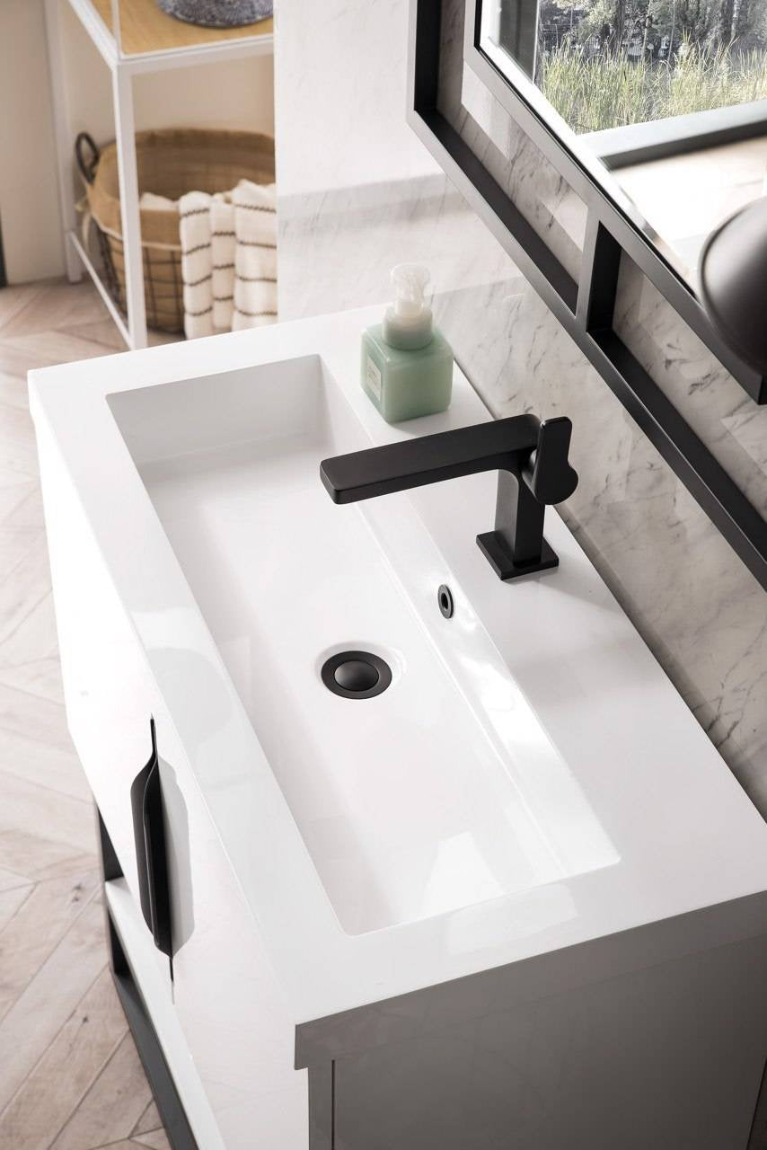 Overhead view of a modern single-sink bathroom vanity with a white integrated stone countertop sink, matte black single-handle faucet and drain, black cabinet handle and solid wood base against a marble backsplash.