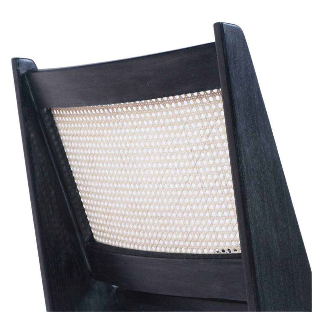 Close-up of a lounge chair back featuring a natural woven cane panel framed by a smoked black solid teak wood frame, highlighting the mid-century modern low-back angled profile.