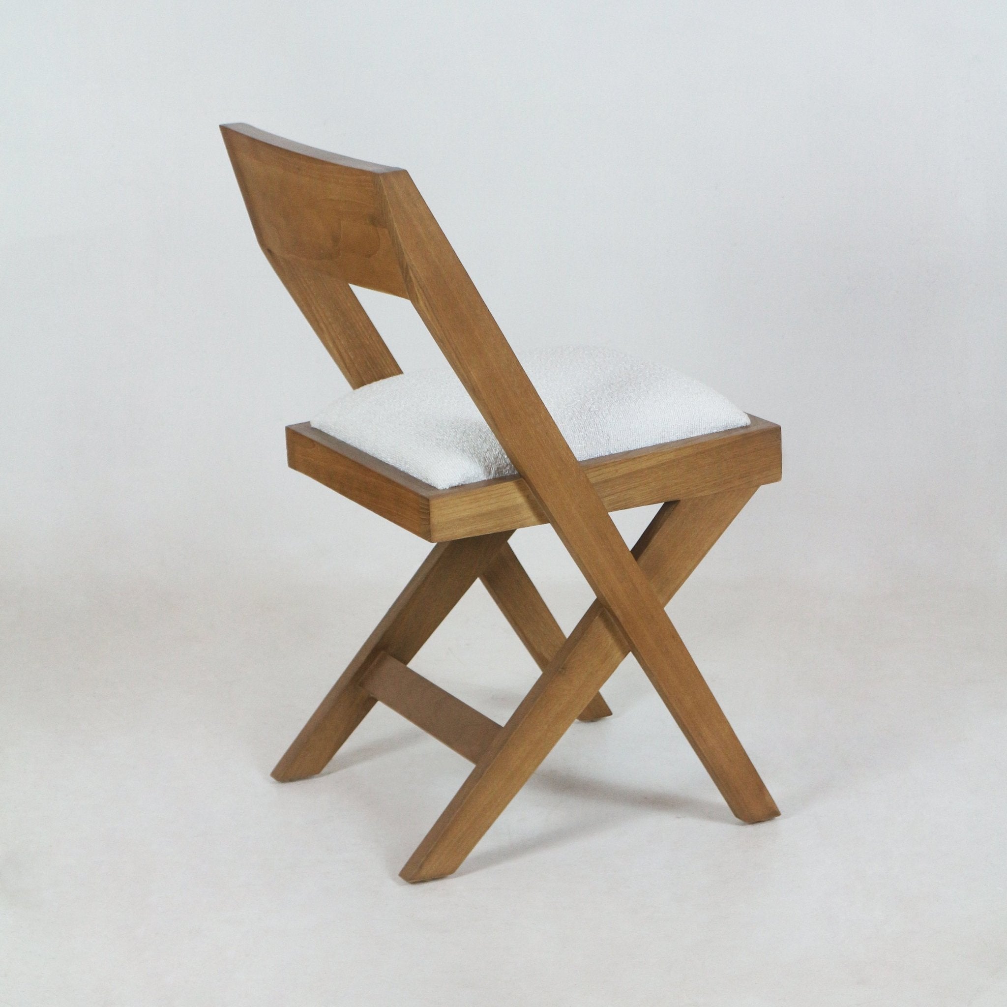 Armless side chair with a warm teak natural wood frame and white boucle upholstered seat cushion, featuring crossed X-shaped legs and an angled low back in a mid-century modern style.