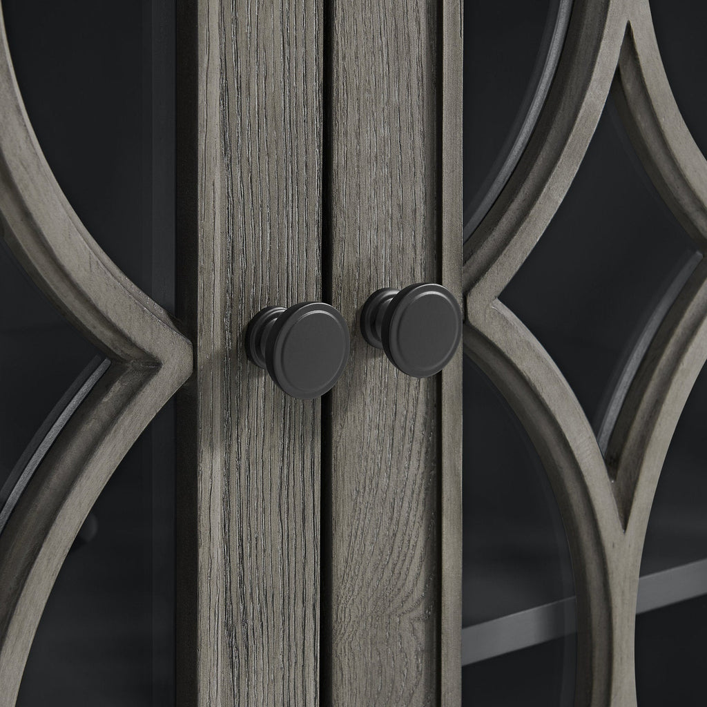 Close-up of stone-colored solid wood vanity doors with visible wood grain, decorative curved wood mullions over glass panels, and two matte black round cabinet knobs.