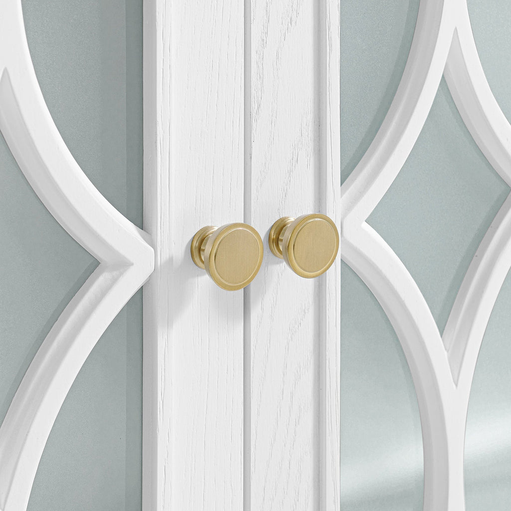 Close-up of white solid wood double vanity doors with carved decorative overlay and two round brushed-gold knobs set against stone-colored glass panels.